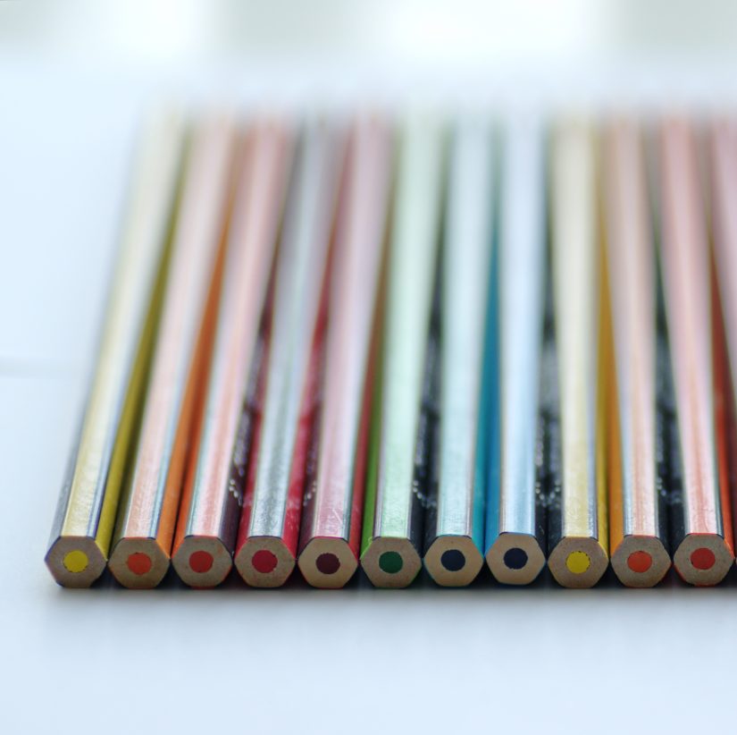 An incredibly neat and organized row of coloured pencils sit together on a table.